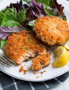 Two salmon patties on a white serving plate with a side of salad.