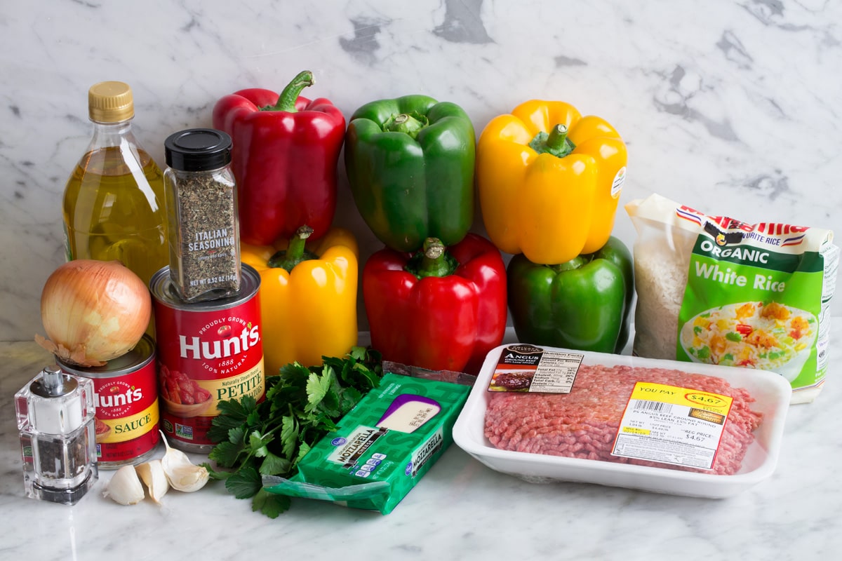 Ingredients to make stuffed peppers show here including bell peppers, ground beef, tomato sauce, diced tomatoes, garlic, onion, italian seasoning, mozzarella, white rice, olive oil, parsley.