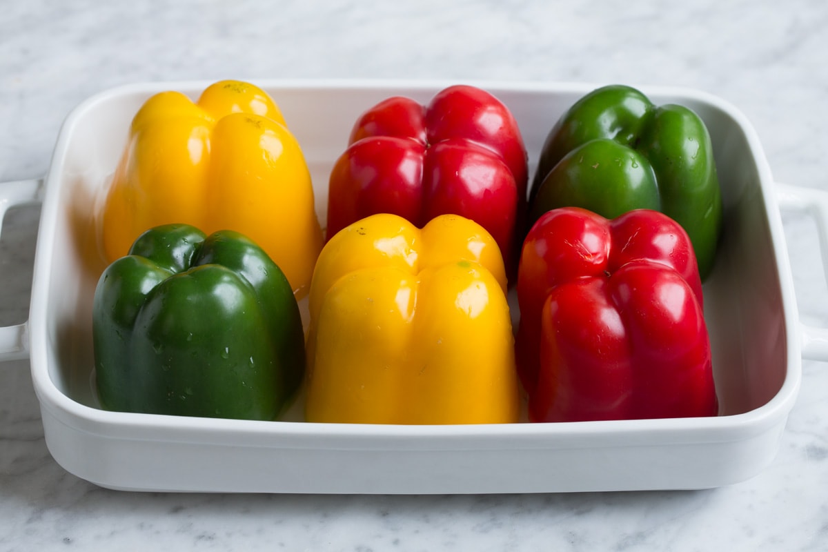 6 multicolor bell peppers in a white baking dish.