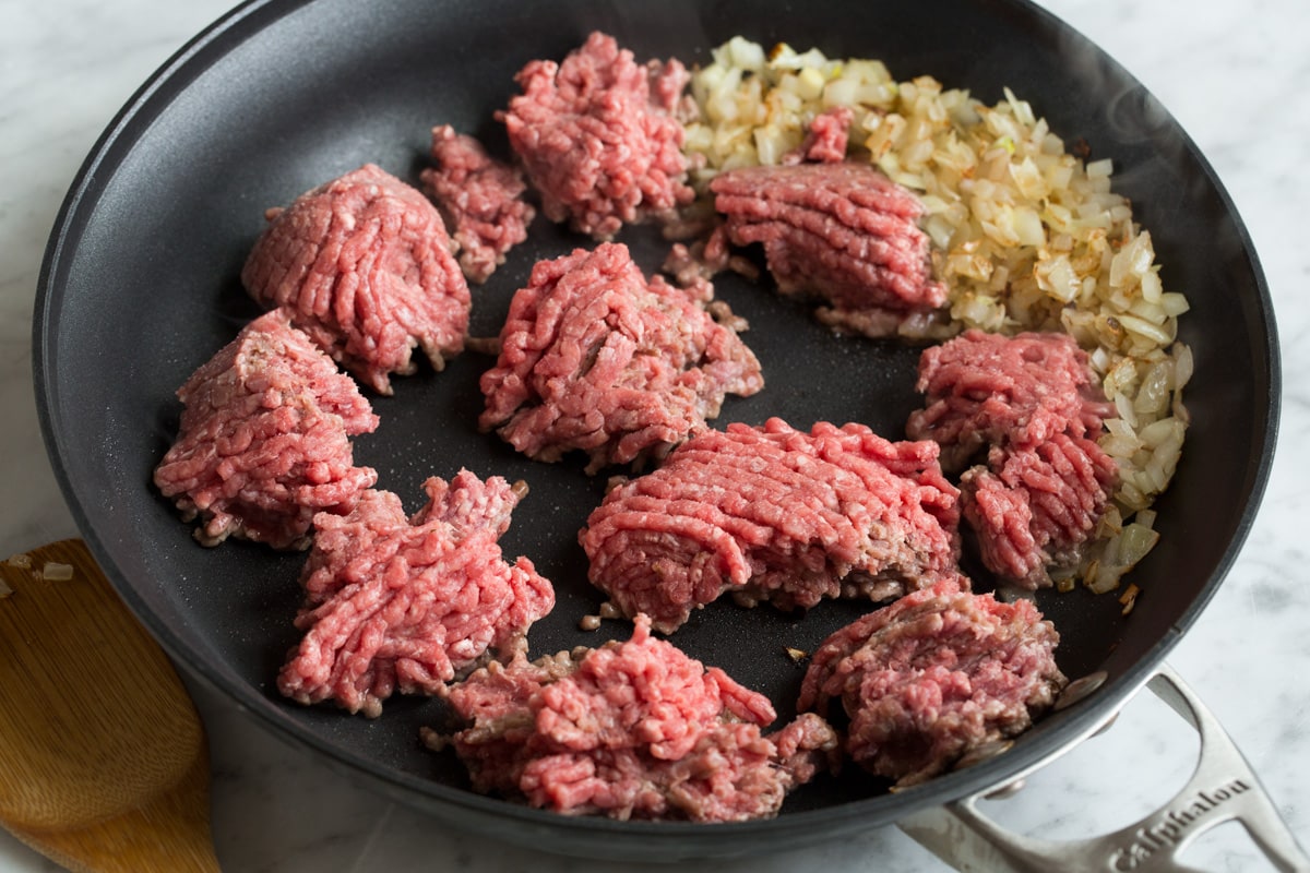 Showing how to make stuffed peppers, browning ground beef in a skillet along with yellow onions.