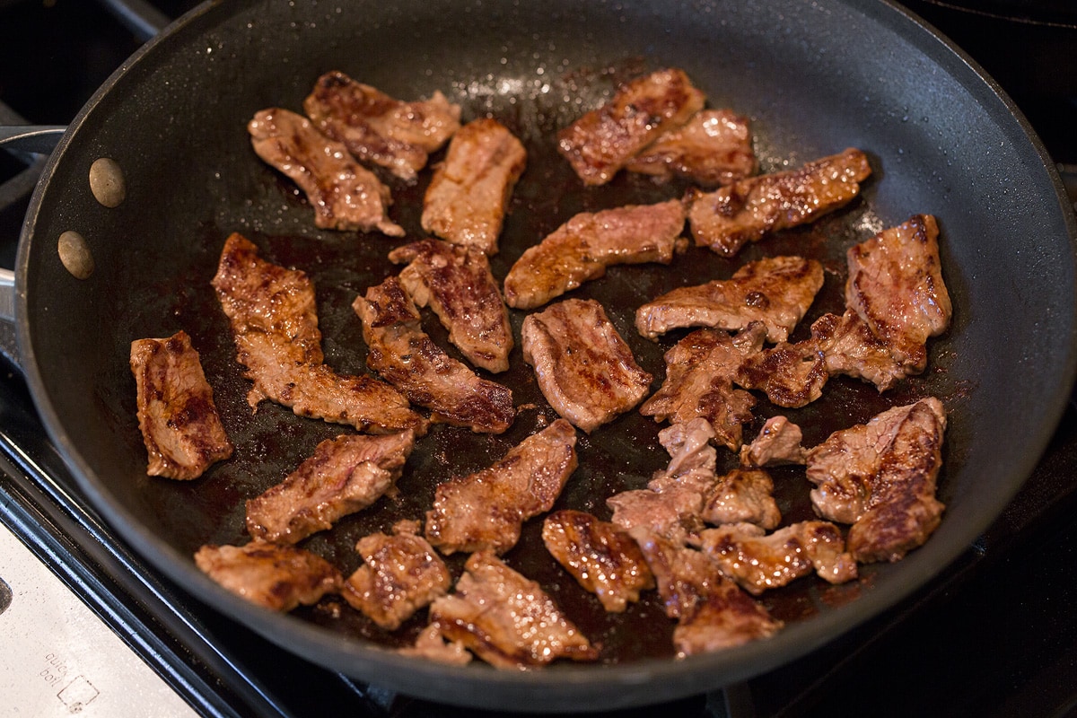 Sliced steak strips cooking in a skillet.