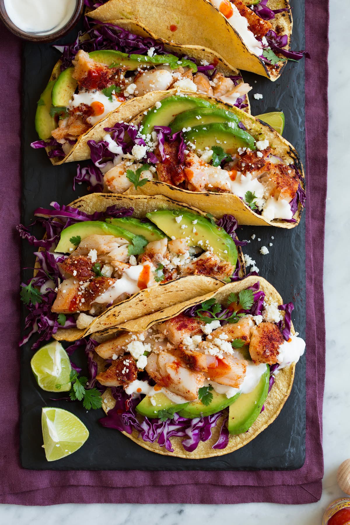 Row of fish tacos on a black slate serving platter.