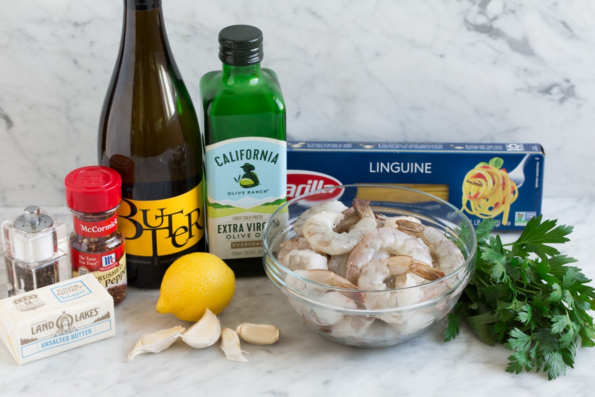 Shrimp scampi ingredients shown here including shrimp, wine, lemon, garlic, butter, olive oil, shrimp, parsley, red pepper flakes, salt and pepper, and pasta.