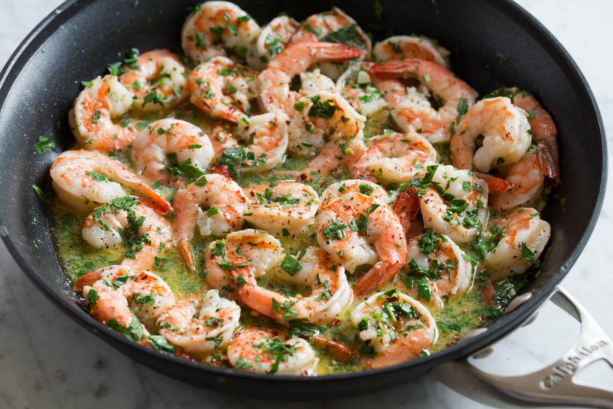 Herbs added to shrimp scampi in skillet.