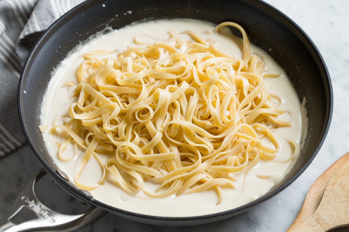 Cooked fettuccine pasta over alfredo sauce in skillet before tossing.