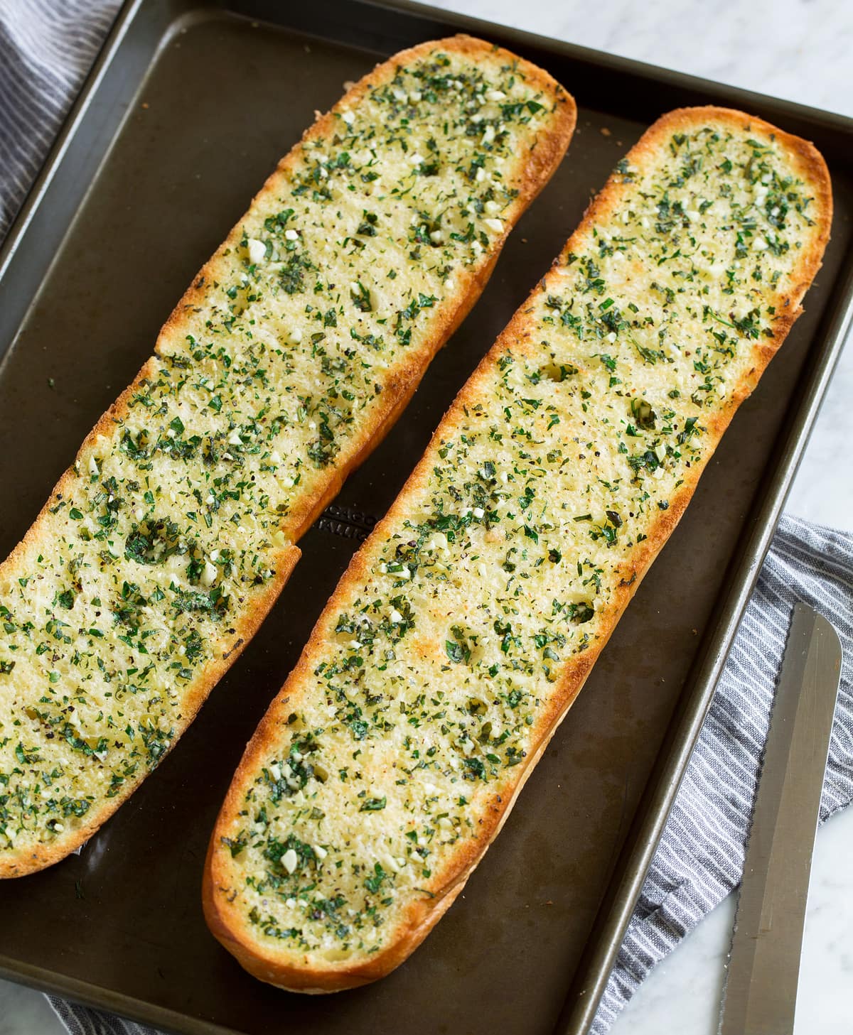 Two garlic bread halves on a dark baking sheet. Shown after toasting.