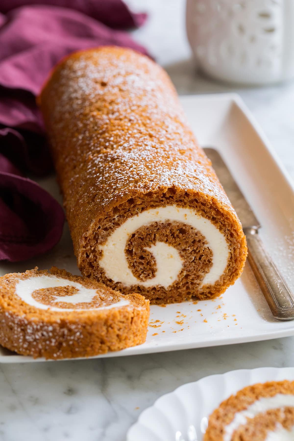 Pumpkin Roll on a white platter with a slice cut to show swirled cream cheese filling.