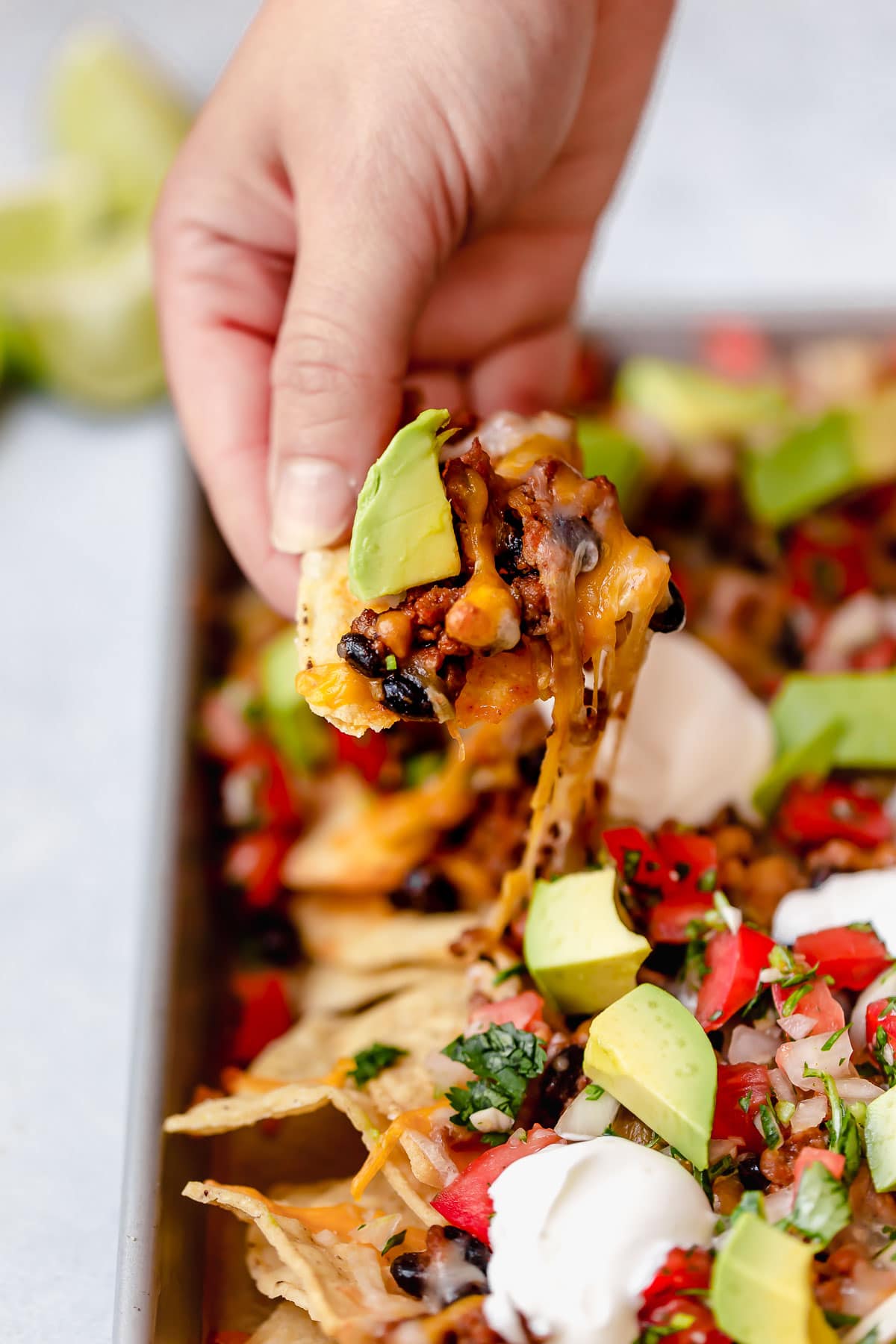 Hand holding nacho chip with melted cheese.