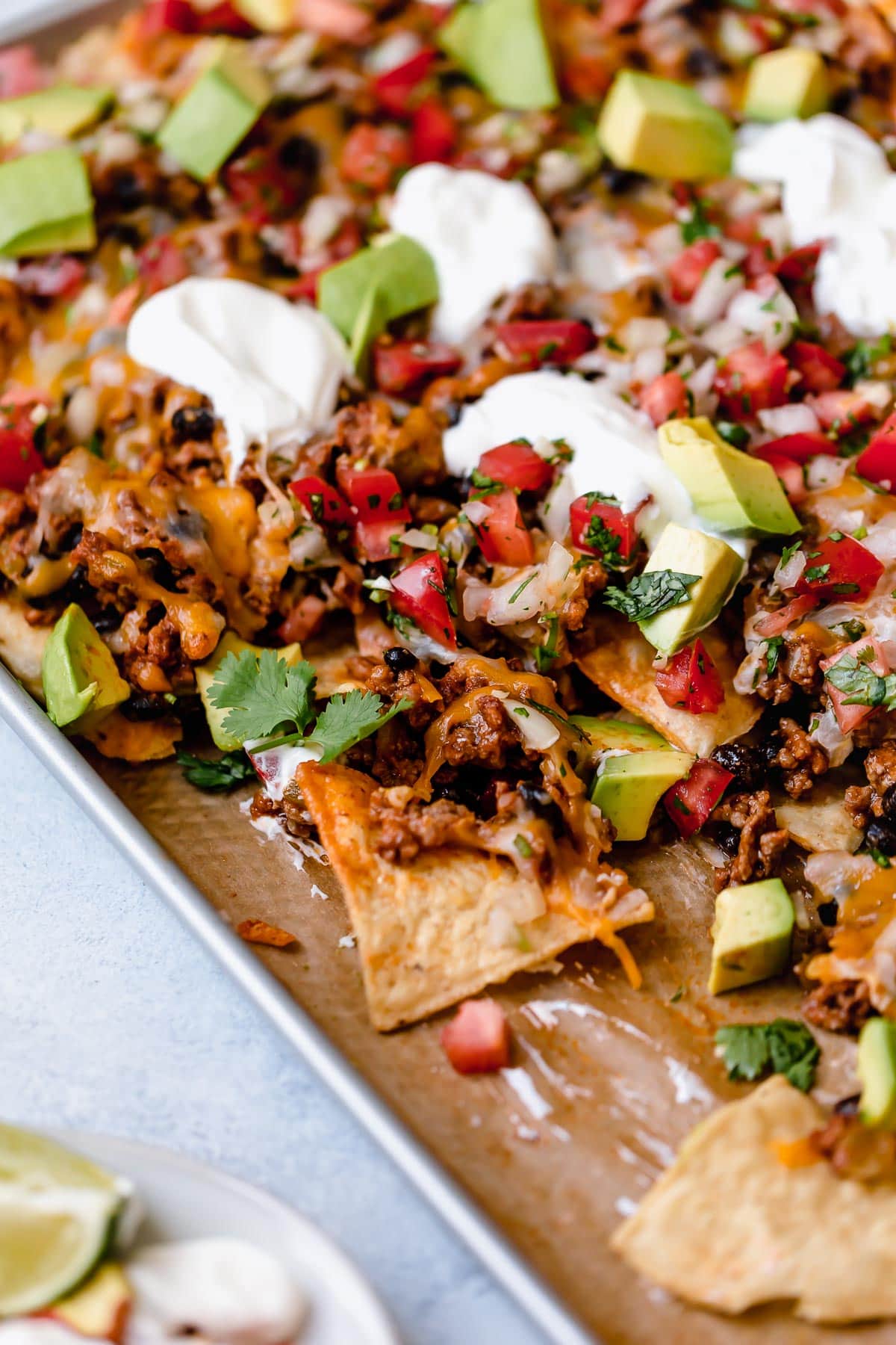 Nachos on a baking sheet with beef, black beans, cheese, pico, and sour cream.