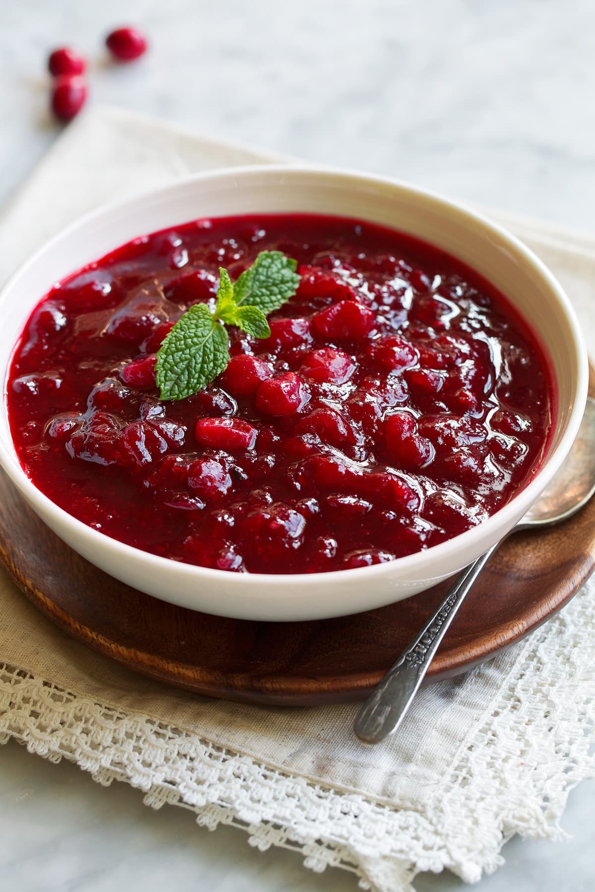 Cranberry Sauce in a serving bowl set over a wooden platter. Sauce garnished with fresh mint.