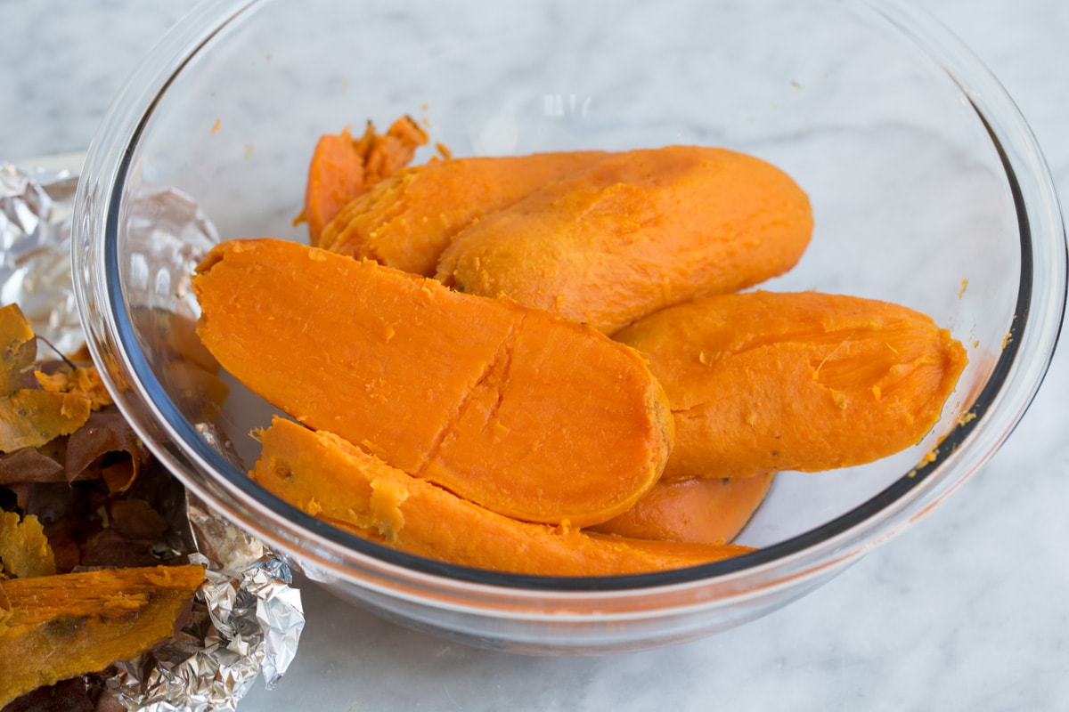 Baked skinless sweet potatoes halves in a large glass mixing bowl. Showing how to make mashed sweet potatoes.