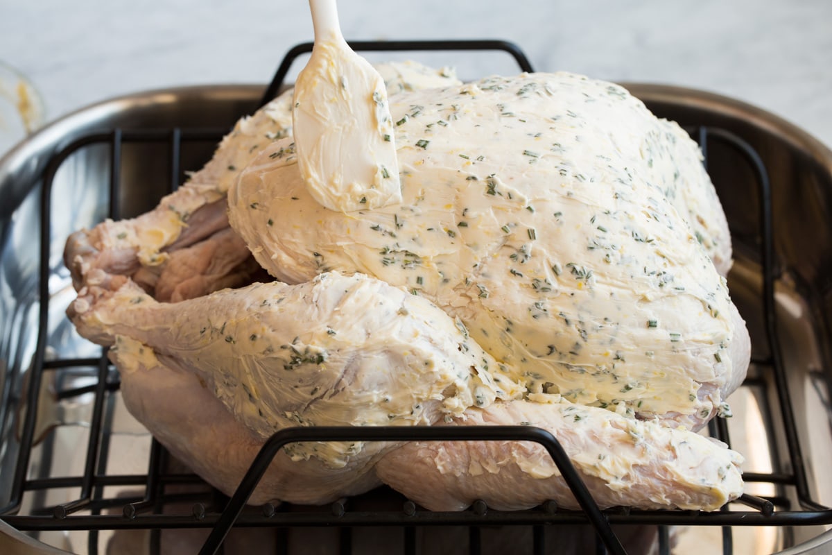 Showing how to prepare a turkey for roasting. Brushing herb butter on large turkey in a roasting pan using a spatula.