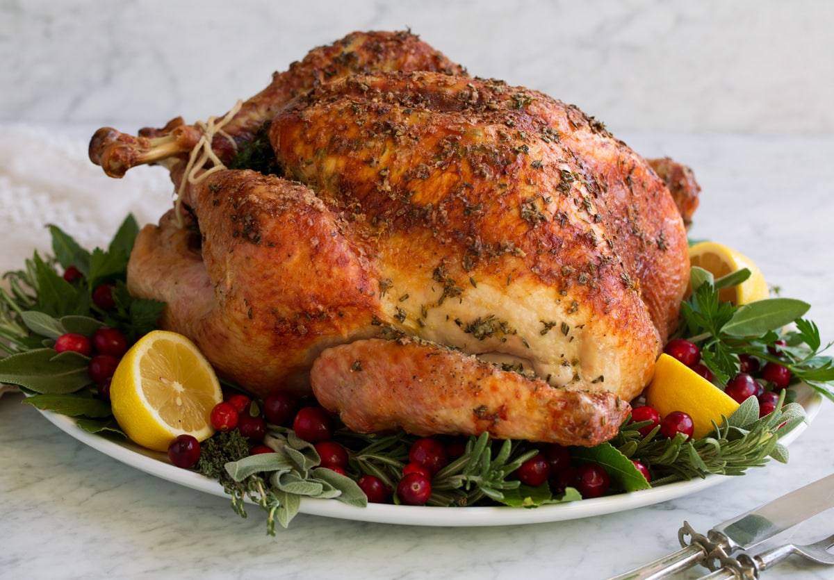 Whole roasted turkey on a serving platter with herbs lemons and cranberries