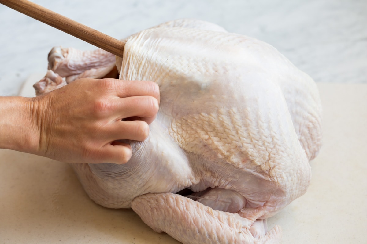 Pressing back end of a wooden spoon into underside of turkey to create space to add butter.