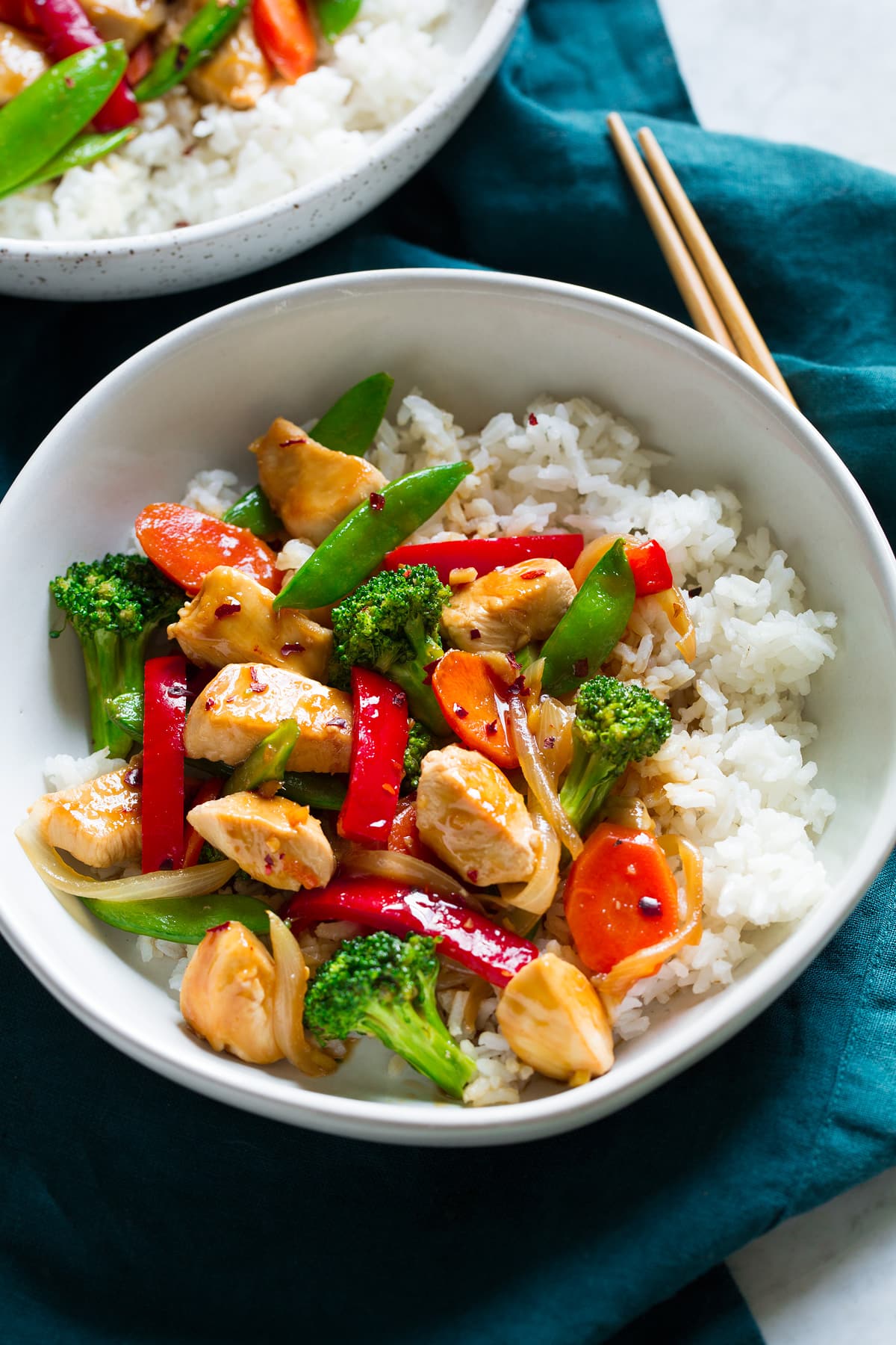 Chicken and vegetable stir fry on white rice in a bowl.