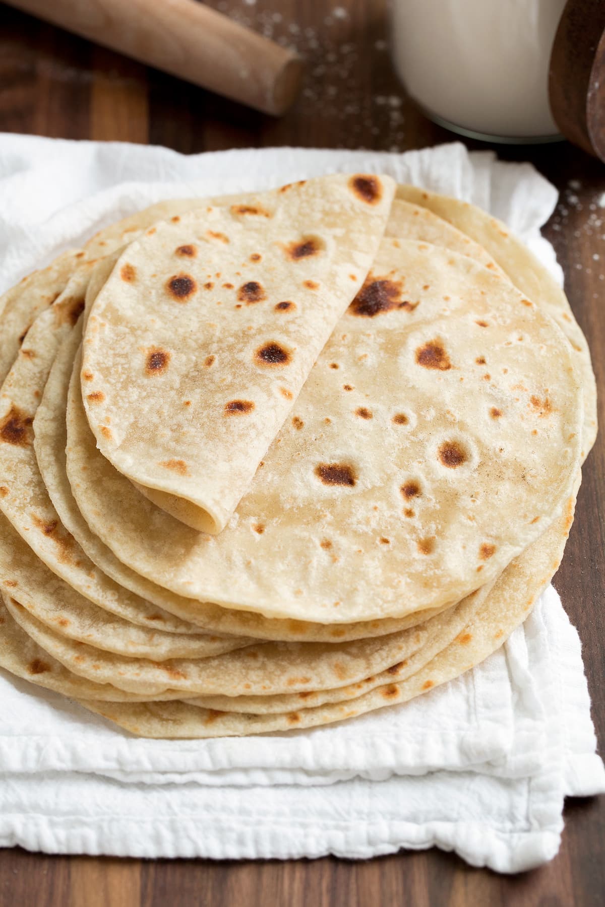 Stack of homemade flour tortillas on a white kitchen cloth. Top tortilla is folded over to show soft and moist texture.