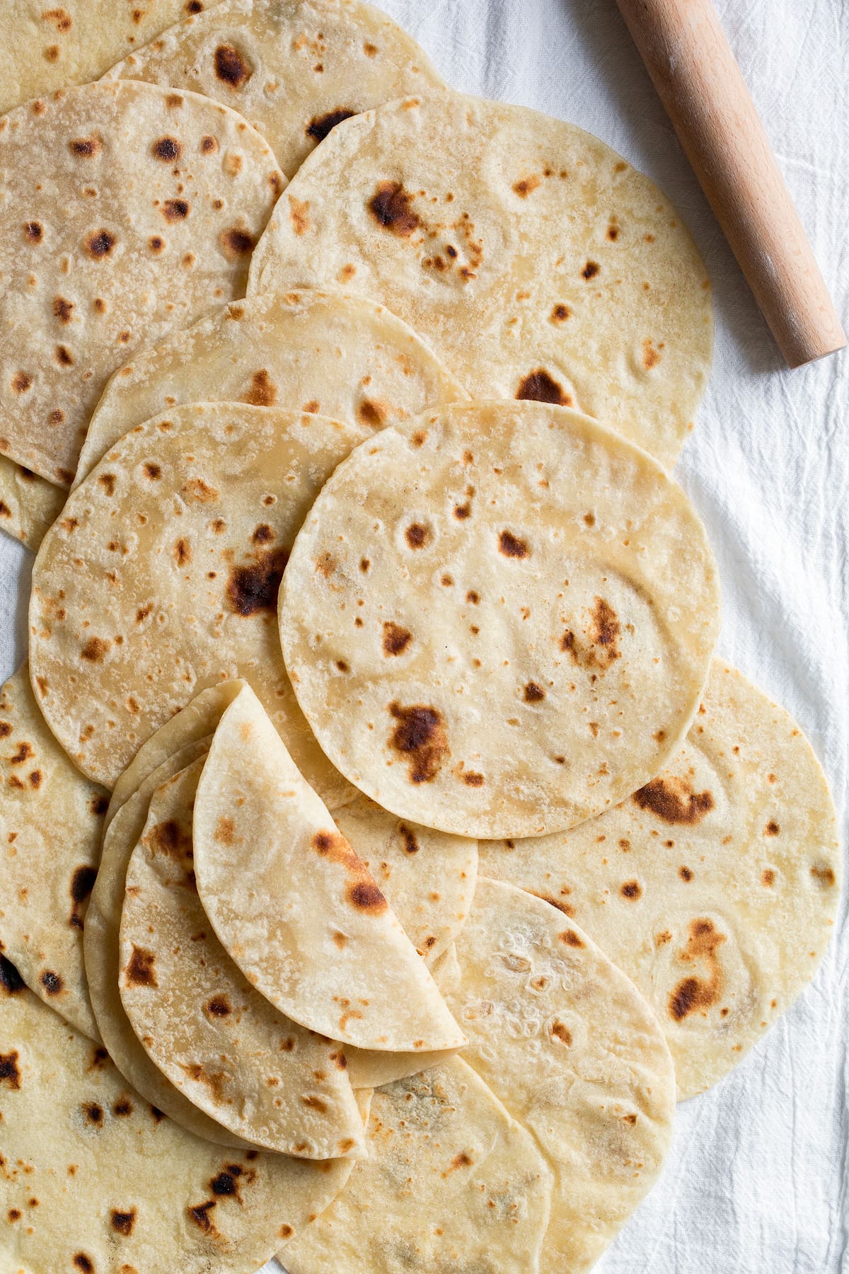 Overhead image of flour tortillas layered across each other on a white kitchen cloth.