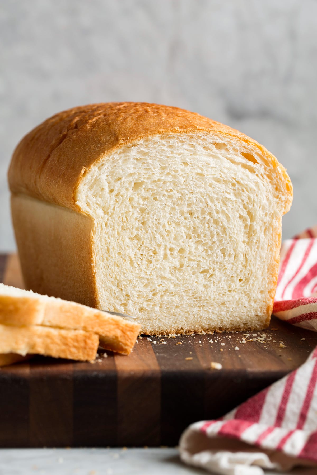 Loaf of white bread on a wooden cutting board with two slices cut. Shows interior of bread.