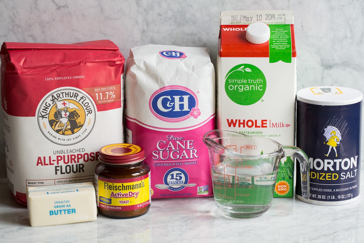 Image of ingredients used to make white bread. Includes all-purpose flour, sugar, milk, salt, water, yeast and butter.