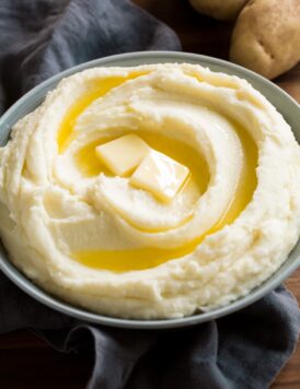 Mashed potatoes in a grey serving bowl over a grey napkin. Potatoes are topped with butter, shown as a serving suggestion.