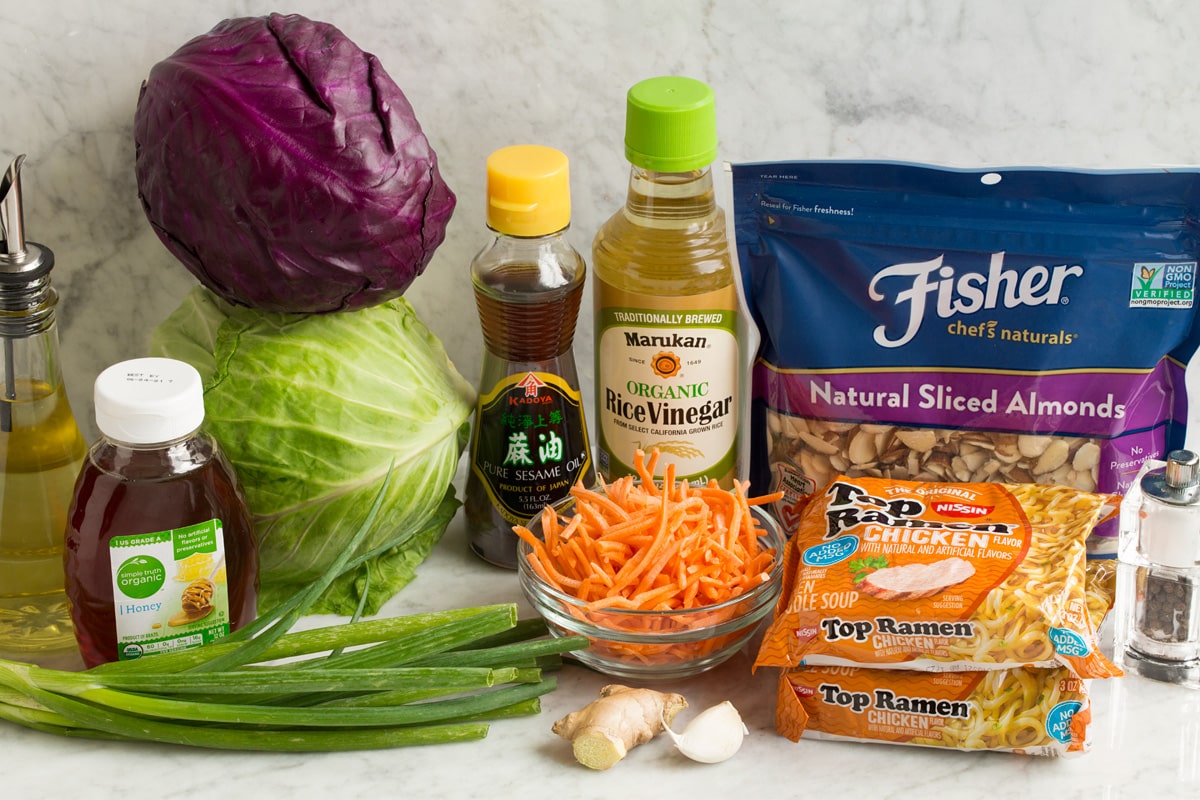 Ingredients used to make Asian ramen noodle salad shown in this image. Includes red and green cabbage, carrots, almonds, dry ramen noodles, honey, rice vinegar, sesame oil, garlic, ginger and oil. 