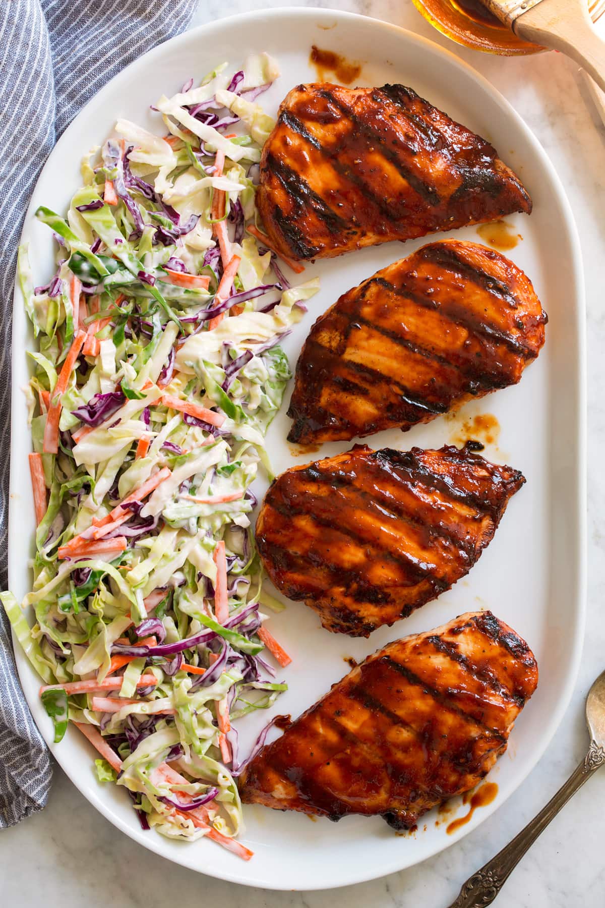 Overhead image of four grilled chicken breasts covered in bbq sauce on a platter with a side of coleslaw on the side of the platter.