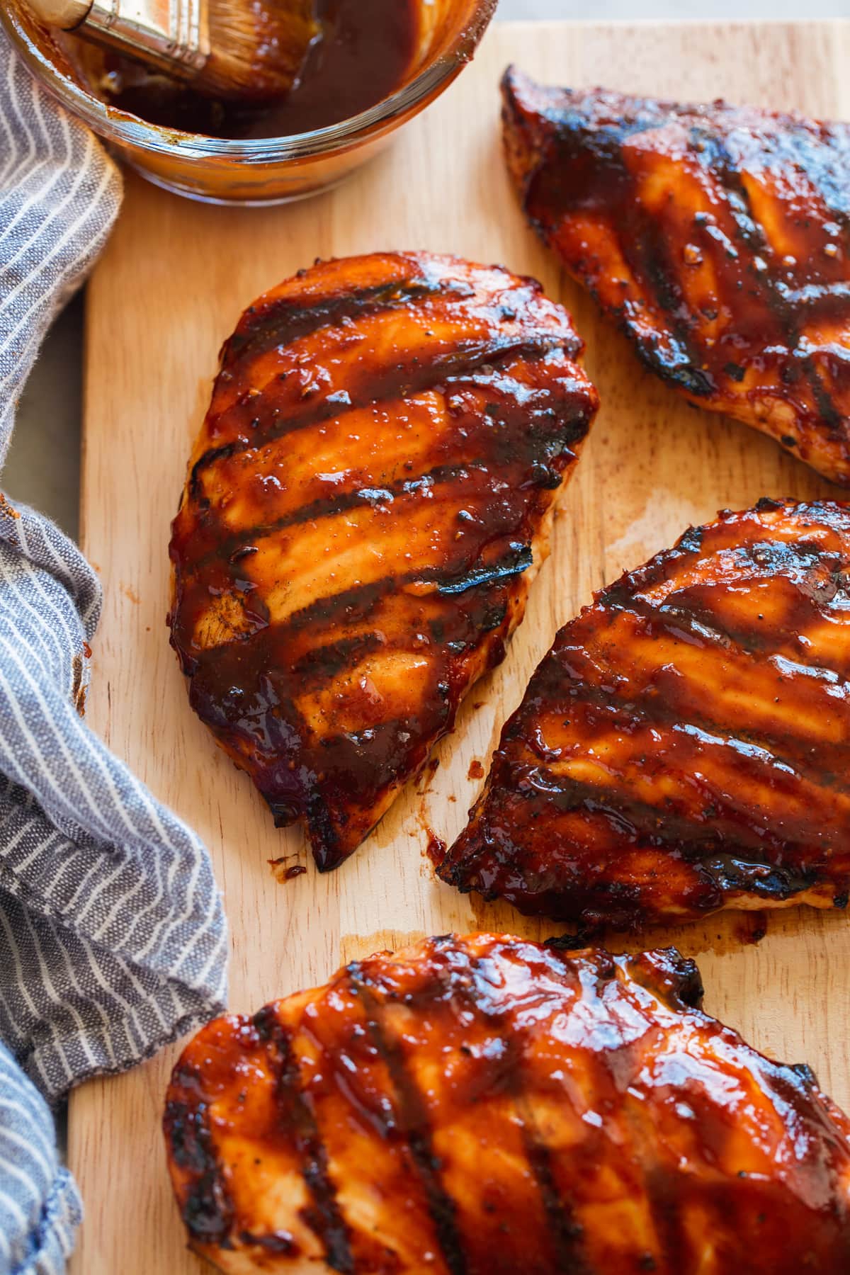 Grilled chicken breasts covered in bbq sauce on a wooden cutting board.