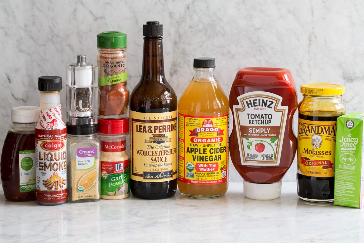 Image of ingredients used to make homemade bbq sauce shown. Including honey, liquid smoke flavor, dry mustard, salt and pepper, garlic powder, smoked paprika, Worcestershire, apple cider vinegar, ketchup, molasses and apple juice. 