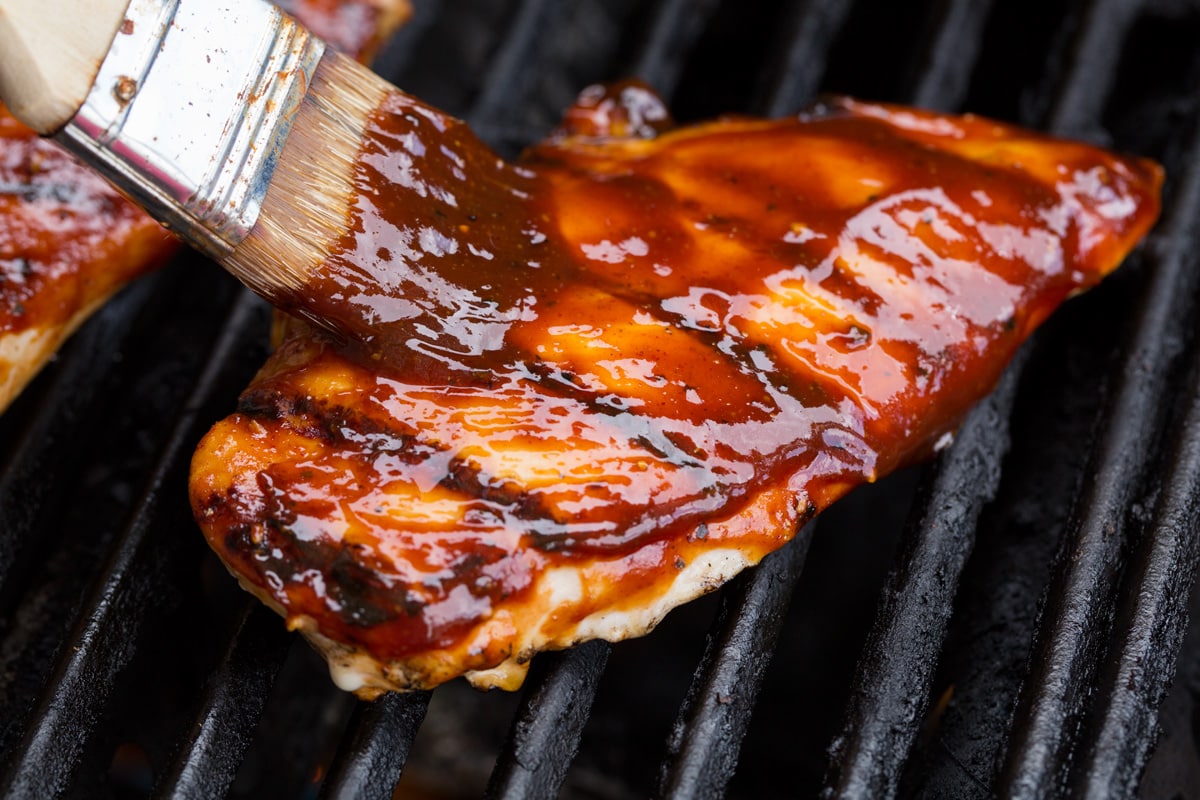 Basting chicken breast on grill with bbq sauce.