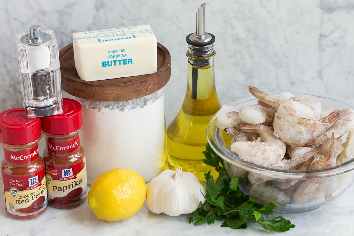 Image of ingredients used to make Hawaiian garlic shrimp. Includes raw shrimp, olive oil, parsley, garlic, lemon, flour, butter, paprika, cayenne pepper, salt and pepper.