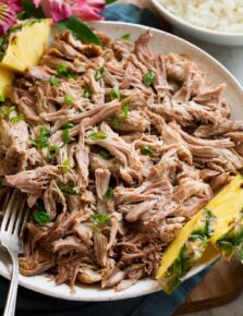 Kalua pork shown in a serving bowl with pineapple and rice to the side.