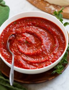 Homemade pizza sauce in a bowl with pizza dough in the background.