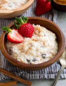 Rice Pudding in a small wooden bowl. It is garnished with cinnamon and strawberries.