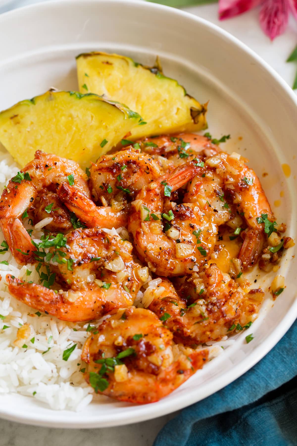 Close up image of Hawaiian garlic shrimp served over white rice with slices of fresh pineapple. 