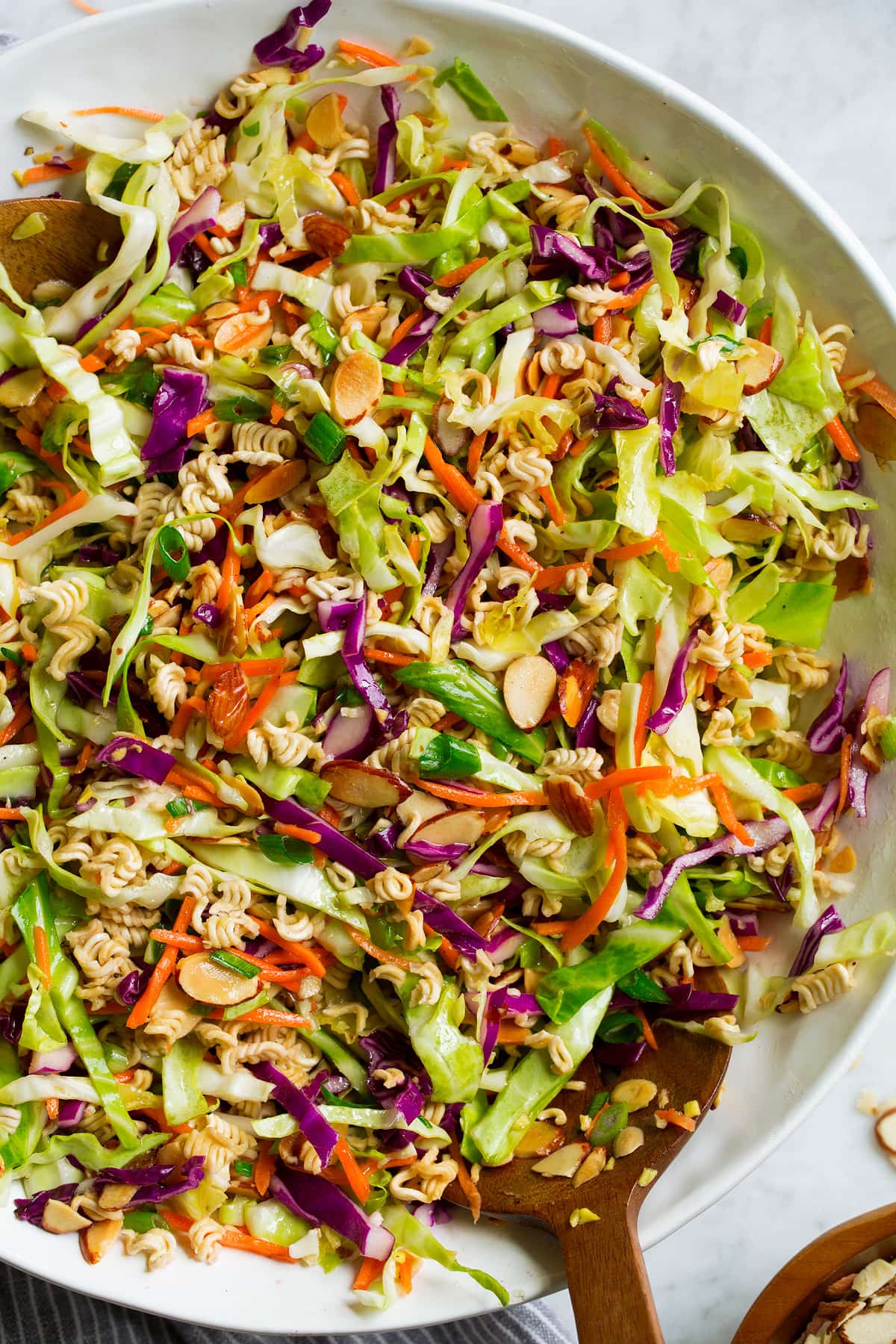 Close up overhead image of Asian ramen noodle salad in a large white salad bowl set over a marble surface.