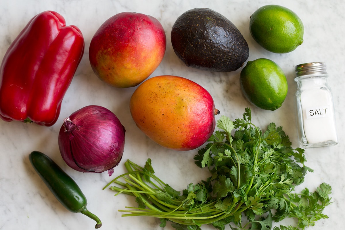 Image of ingredients used in mango salsa. Includes fresh mangoes, avocado, bell pepper, cilantro, red onion, lime, jalapeno and salt.