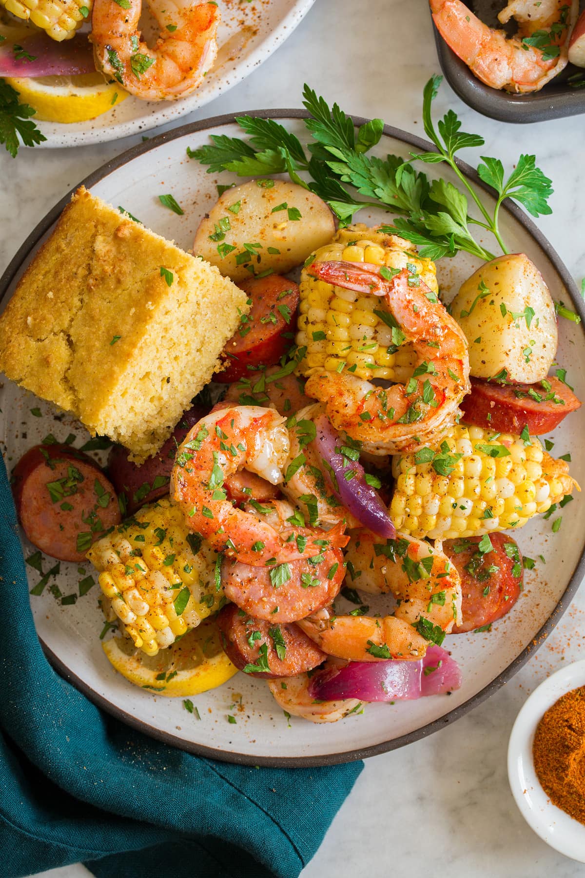 Image showing single serving of shrimp boil on a white plate with a serving suggestion of a side of cornbread.