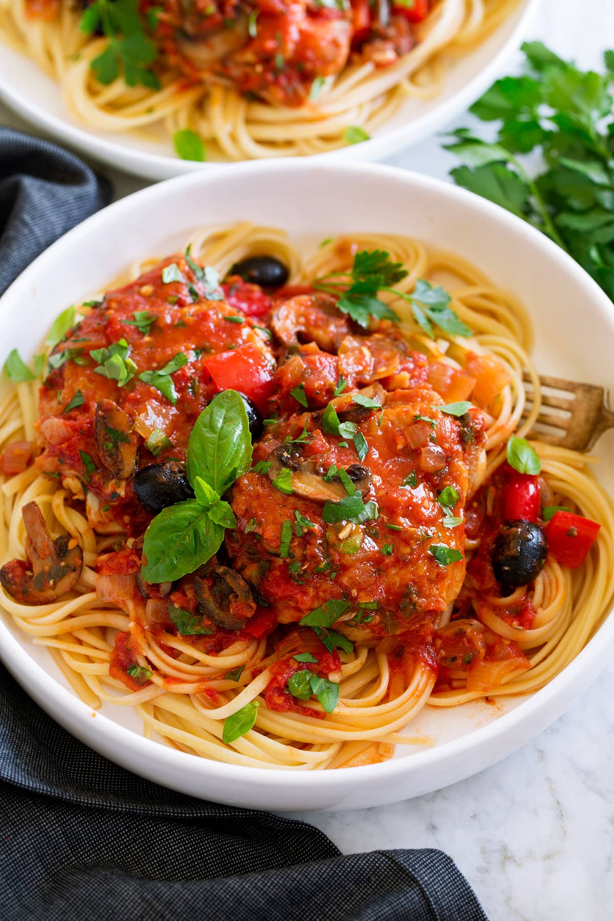 Chicken cacciatore shown served over pasta in a white bowl.