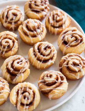 Photo of 12 Mini Cinnamon Rolls shown sitting on white platter over a marble surface.