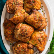 Image of baked chicken thighs shown overhead served on a white oval platter.