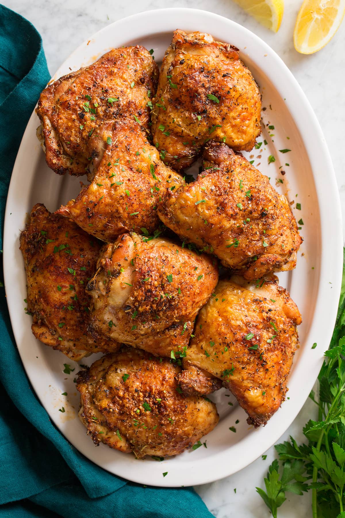 Image of baked chicken thighs shown overhead served on a white oval platter.