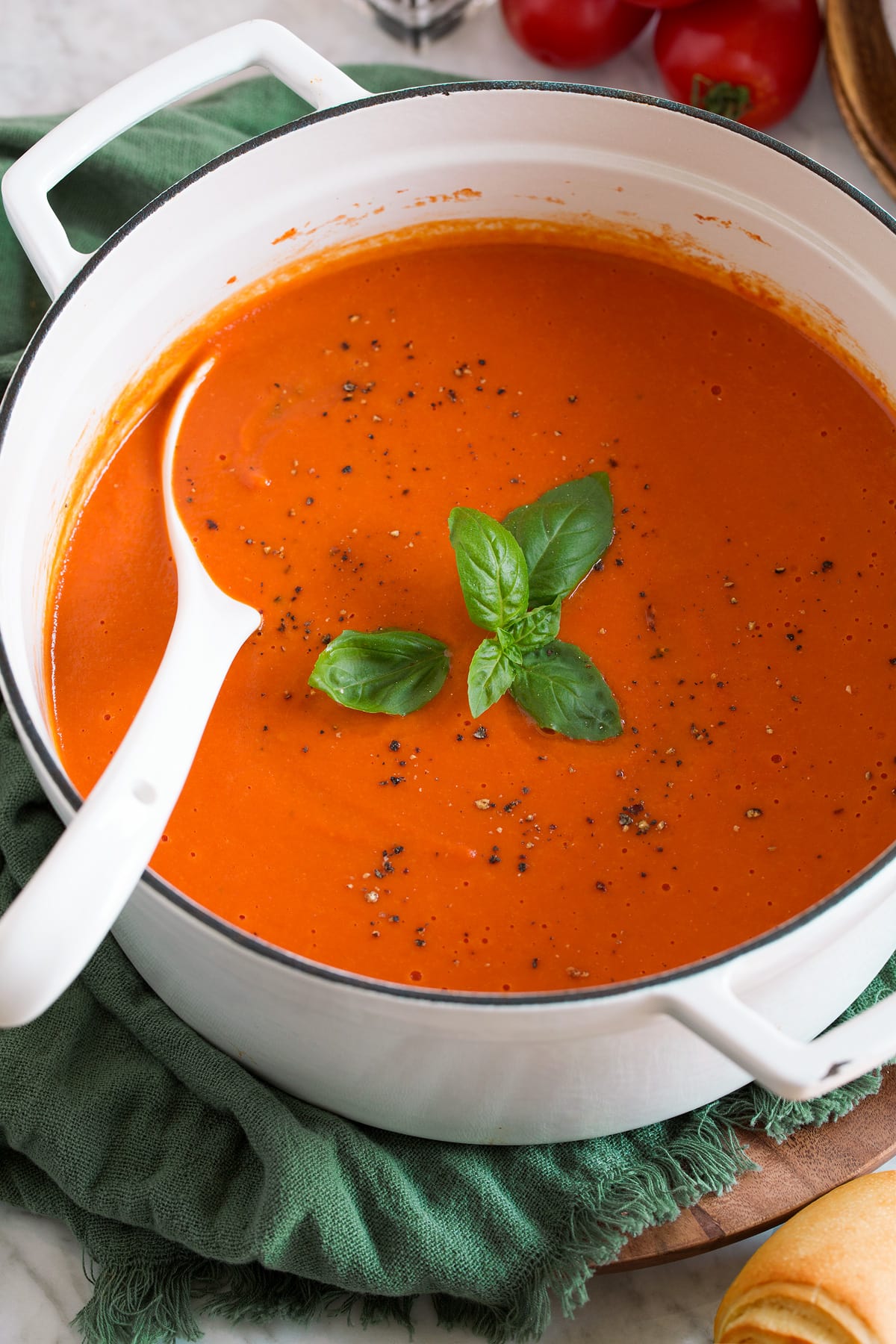 Image of white pot filled with tomato soup that's garnished with basil and pepper.