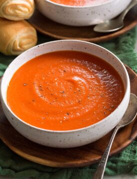 Single serving of tomato soup shown in a white bowl set over a wooden plate.