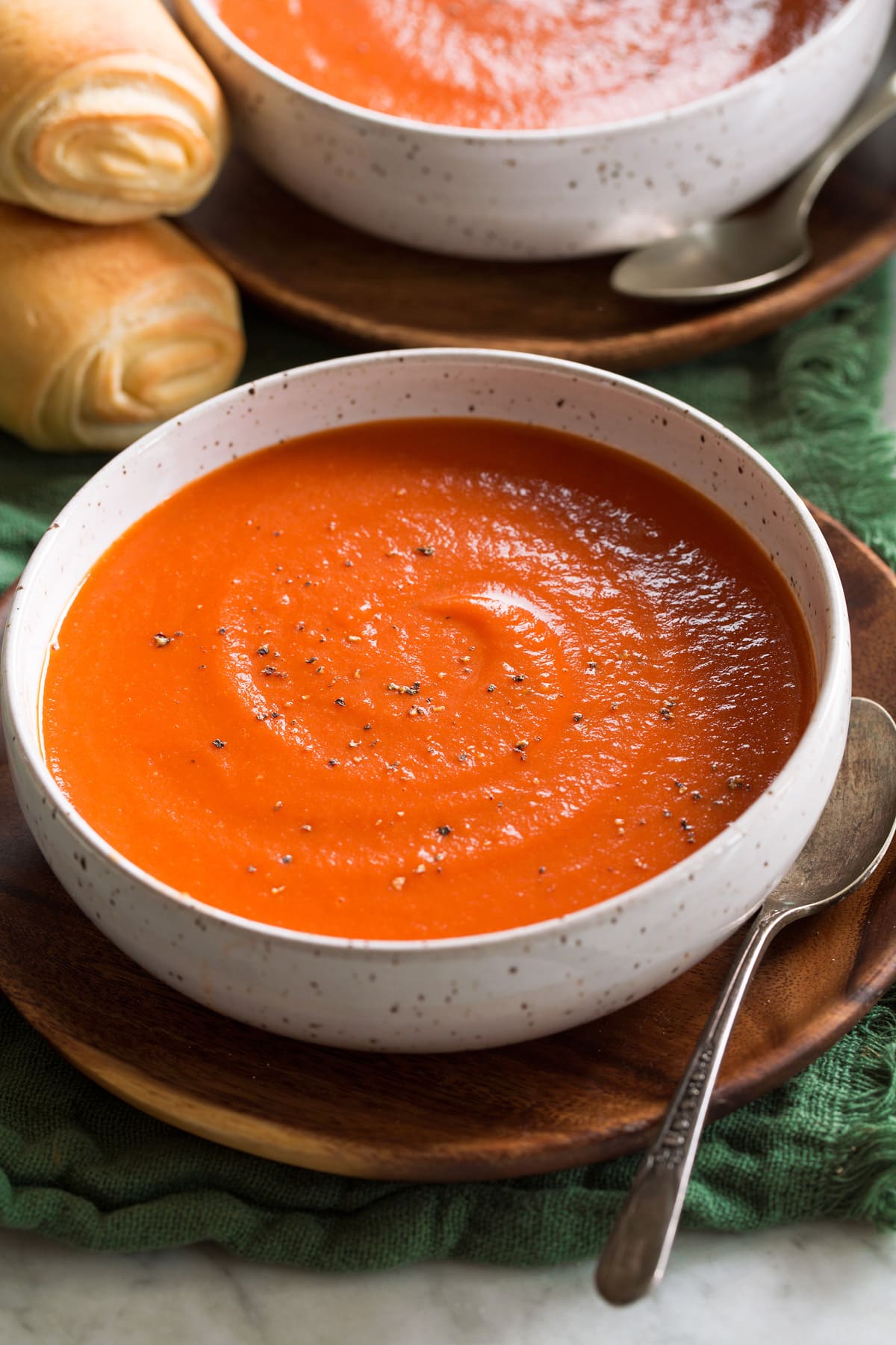 Single serving of tomato soup shown in a white bowl set over a wooden plate.