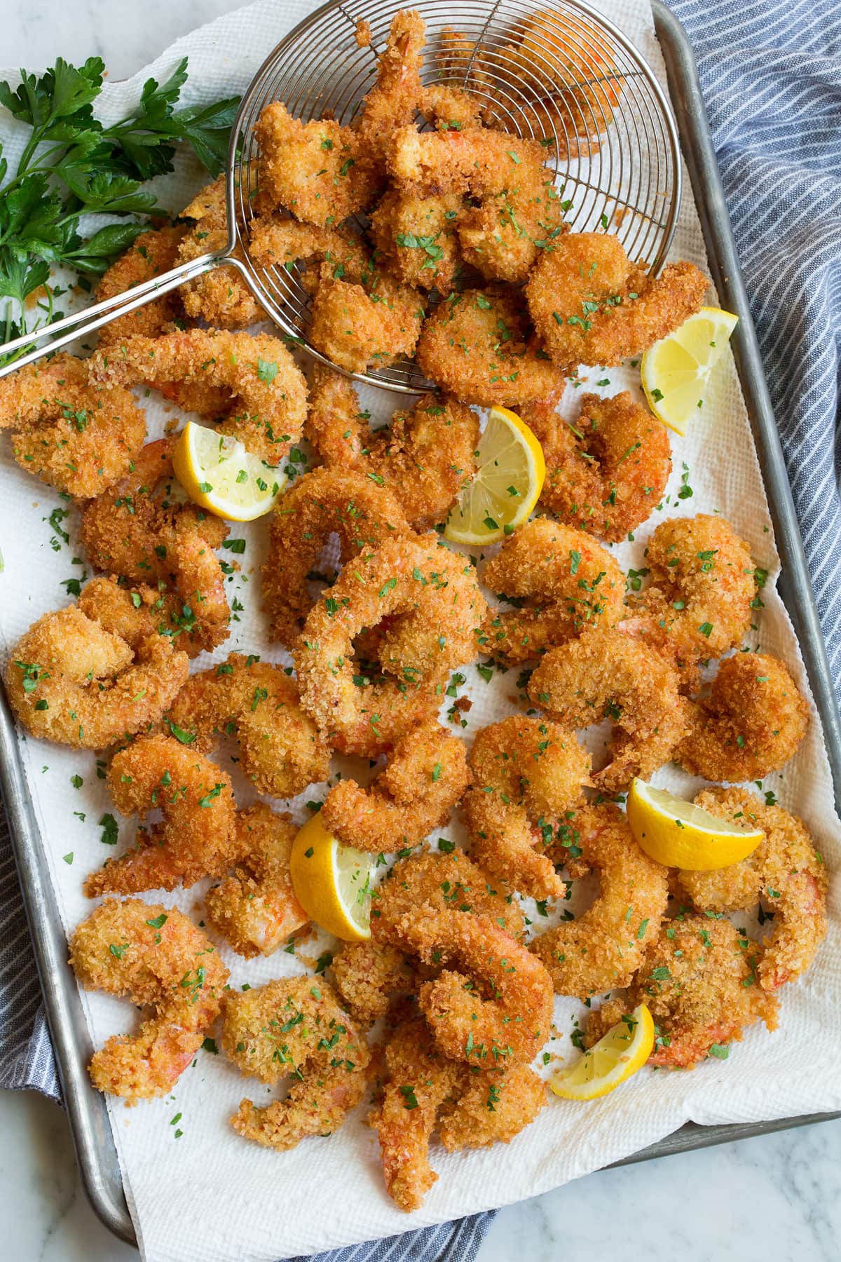 Overhead photo of fried shrimp layered on paper towel lined baking sheet.