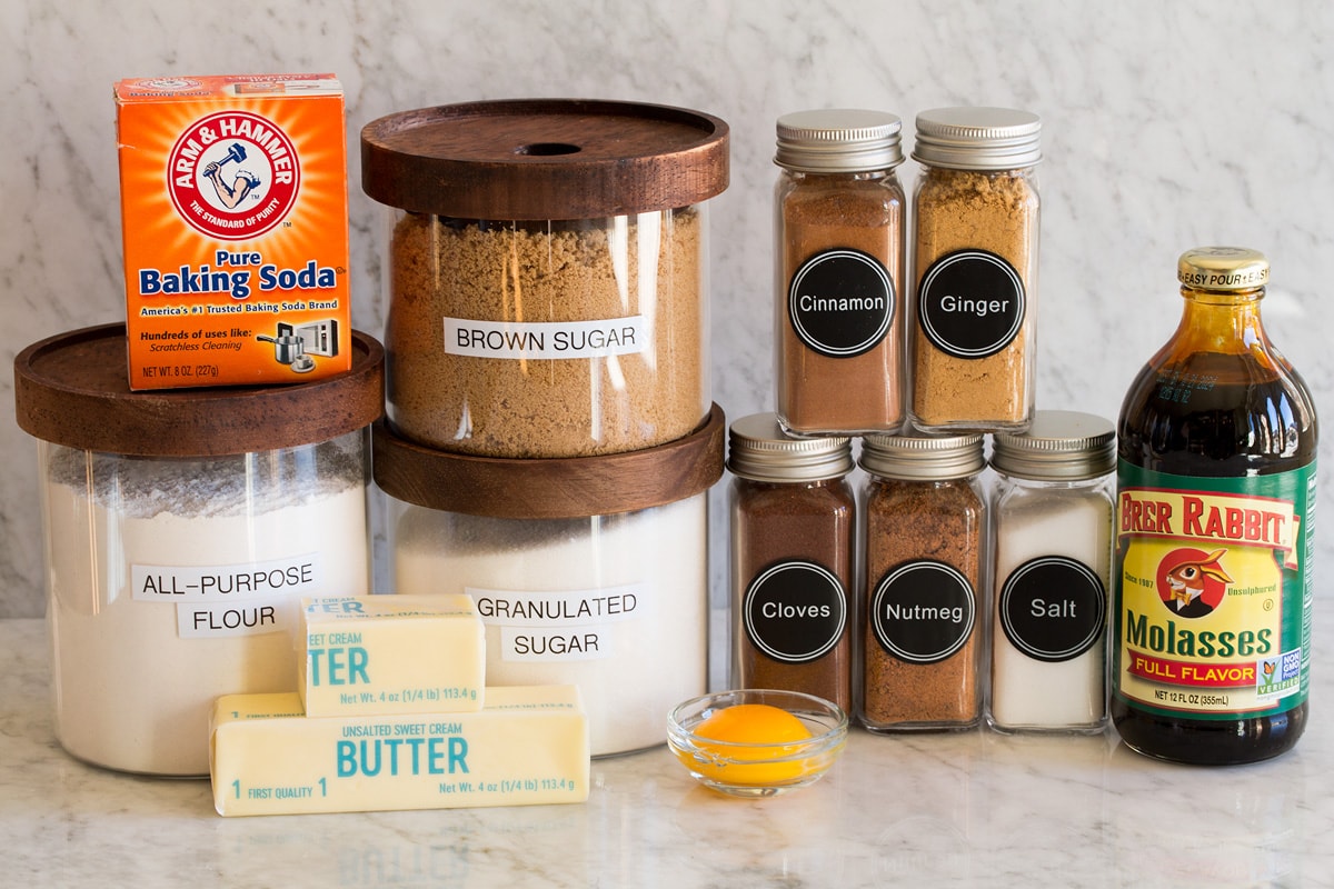 Image of ingredients used to make molasses cookies. Includes flour, sugar, molasses, brown sugar, baking soda, salt, egg yolk, butter, cinnamon, nutmeg, ginger, and cloves.