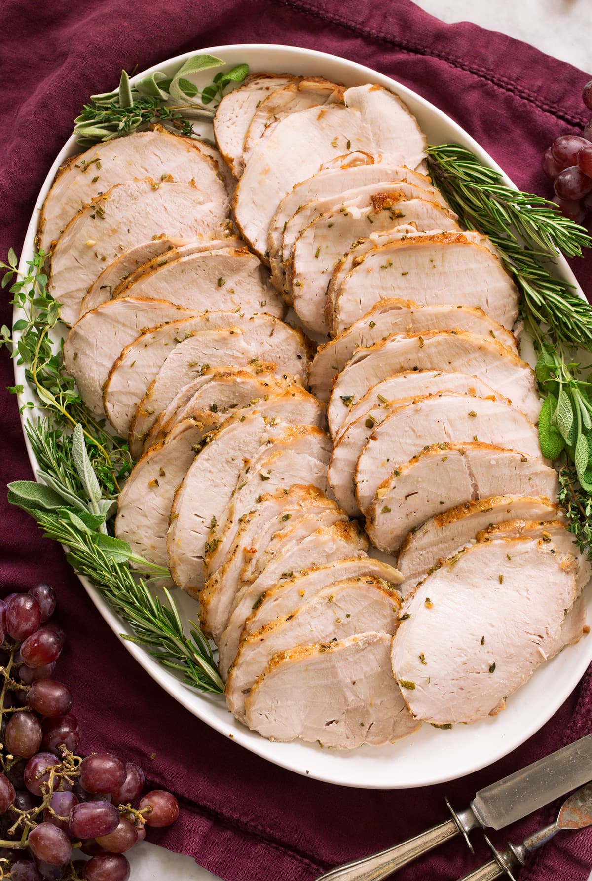 Pork loin shown cooked and thinly sliced on a white oval serving platter over a purple cloth.