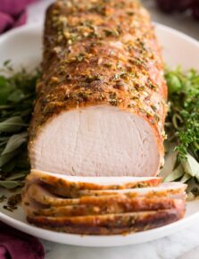 Pork Loin Roast served on a white platter with fresh herbs. Pork is shown sliced at the forefront.