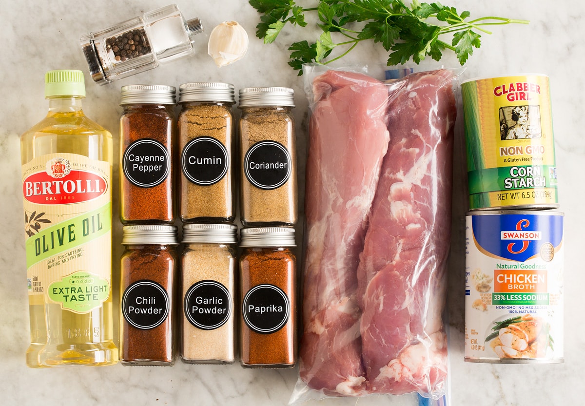 Image of ingredients used to make pork tenderloin. Includes to pork tenderloins, cumin, coriander, paprika, garlic powder, chili powder, cayenne pepper, olive oil, salt and pepper, garlic, parsley, cornstarch and chicken broth.