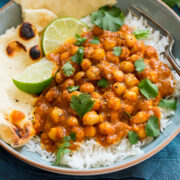 Photo of chickpea curry in a bowl served atop basmati rice with naan bread to the side.